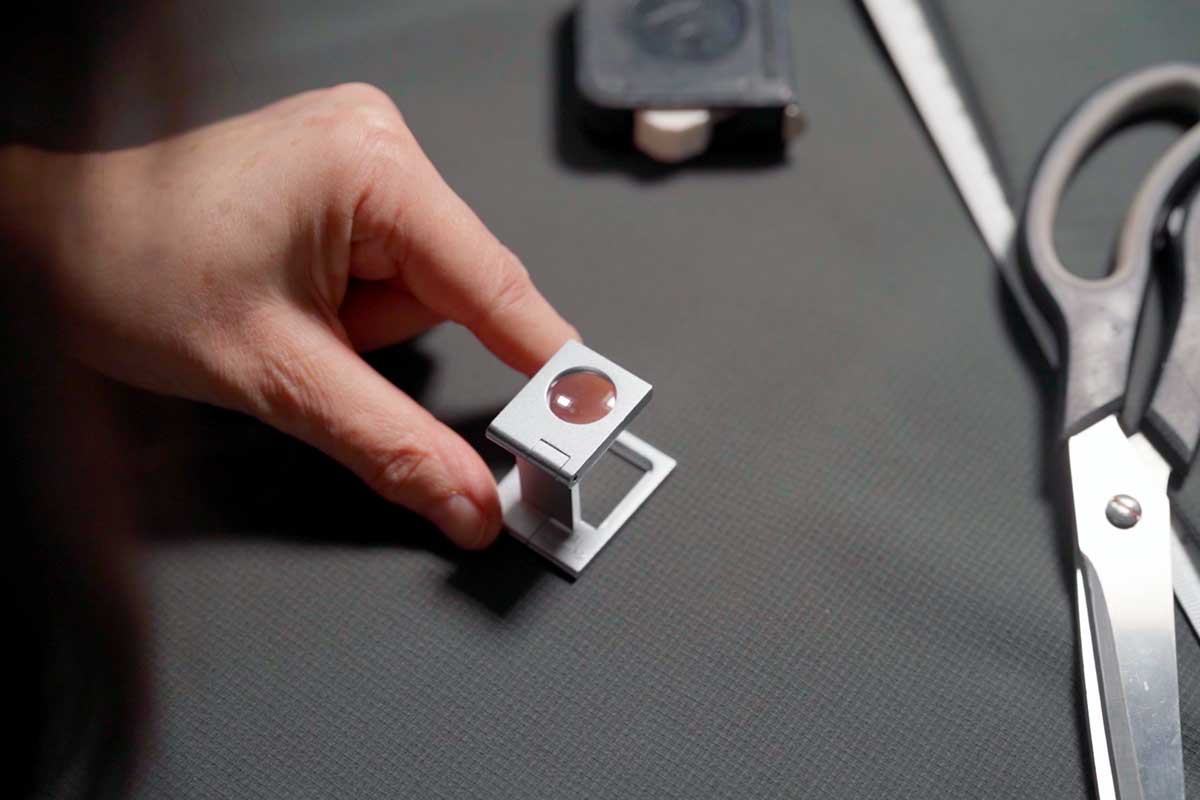Hand prüft Gewebe mit Fadenzähler unter Lupe – Qualitätssicherung bei Spengler & Fürst