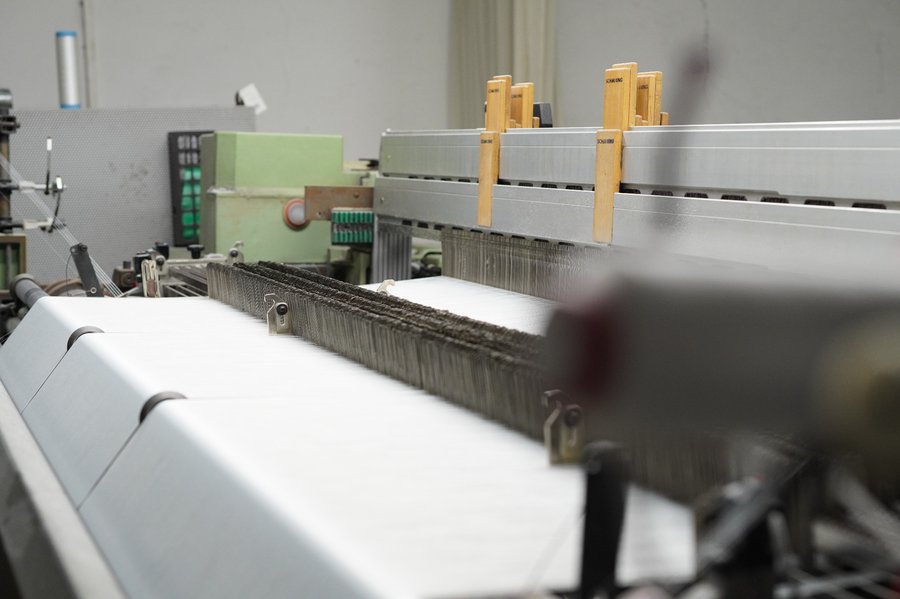 Detailansicht einer Webmaschine bei der Verarbeitung von Glasgewebe