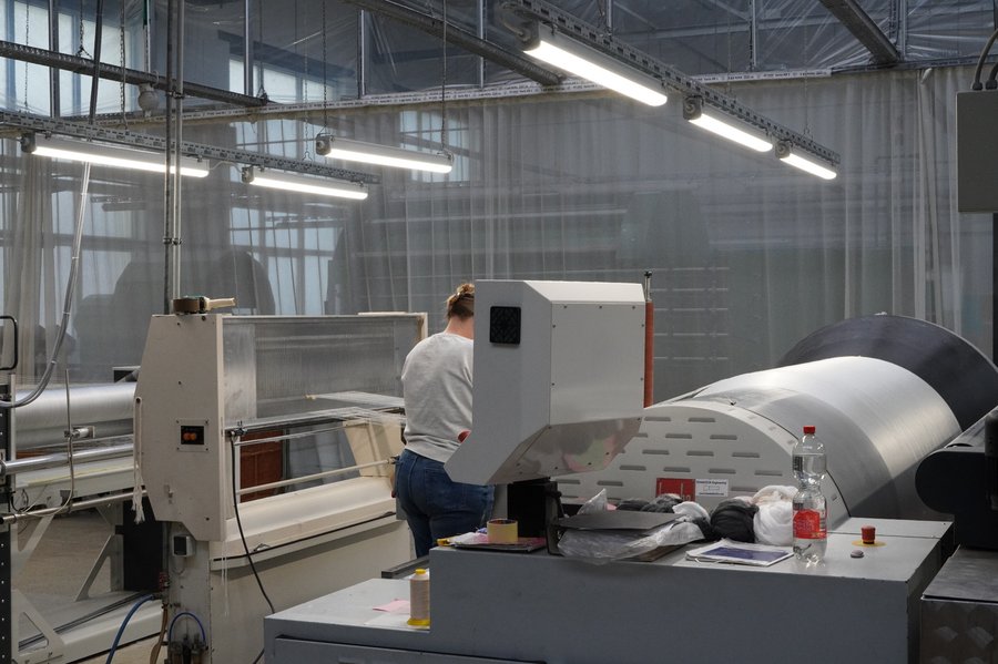 Mitarbeiterin an Maschine zur Herstellung von Geweben für Schutzbekleidung